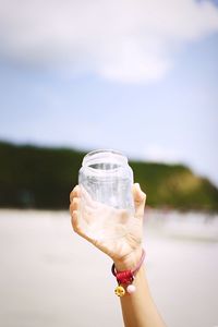 Midsection of person holding drink against sky