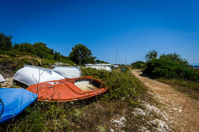 Abandoned boats on field against clear blue sky during sunny day