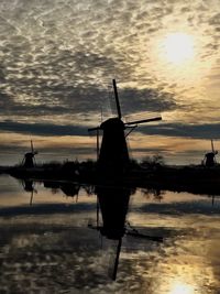 Silhouette cranes on beach against sky during sunset