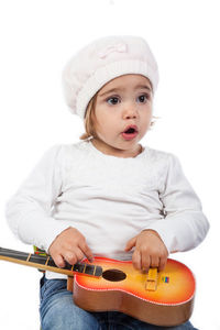Surprised baby girl looking away while holding toy guitar against white background