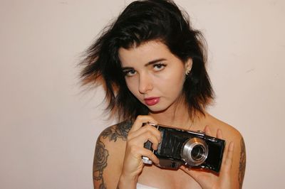 Portrait of woman holding camera against white background