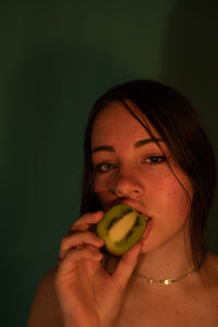 Portrait of woman eating kiwi against wall