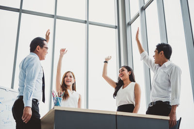 Low angle view of happy business people with hand raised standing in office