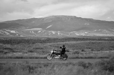 Man riding motorcycle on field against mountains