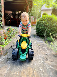 A toddler boy is playing with a toy tractor outdoors. a little cute boy of one and a half years