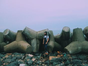 Full length of woman standing by tetrapod rocks against sky