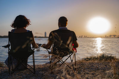 Rear view of people sitting at beach during sunset