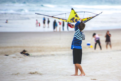 Side view of boy holding kite while standing at beach