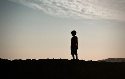 Silhouette boy standing on mountain against sky at sunset