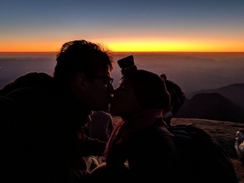 Silhouette couple kissing on mountain against sky during sunset