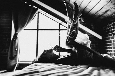 Woman smoking cigarette while lying on bed at home