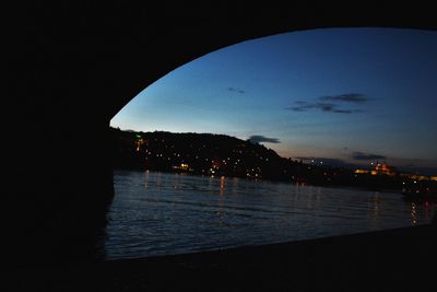 Sea by illuminated city against sky