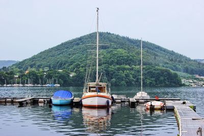 Sailboats moored in river against tree mountain