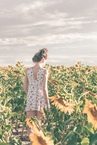 Rear view of woman standing amidst plants against sky 