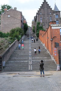 Rear view of people walking on steps amidst buildings in city