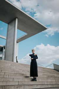 Low angle view of woman gesturing equal sign while standing on staircase against sky