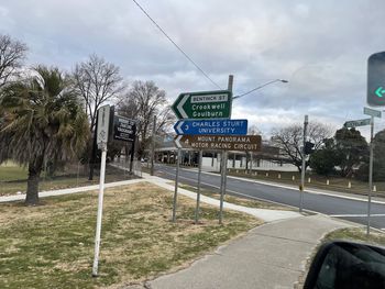 Road sign by trees against sky in city