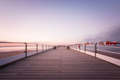 Boardwalk at beach against sky during sunset