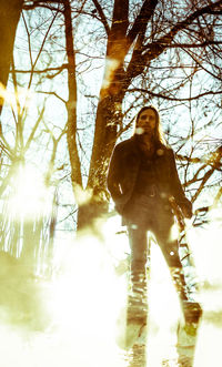 Man standing by bare tree in forest