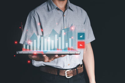 Midsection of man holding camera while standing against black background