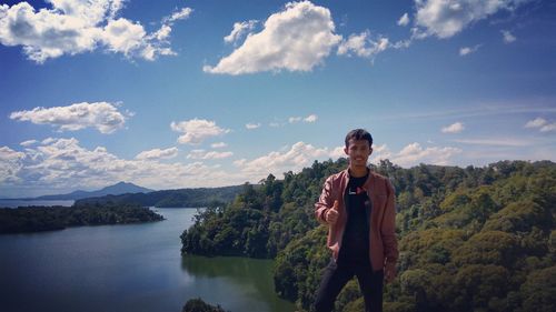 Portrait of smiling young man gesturing thumbs up while standing on mountain against sky 