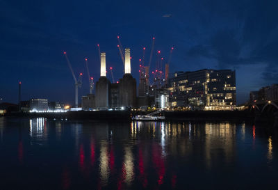 Illuminated city by river against sky at night