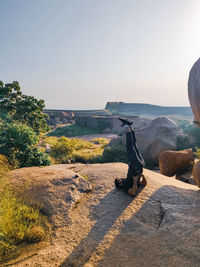 People sitting on rock against clear sky