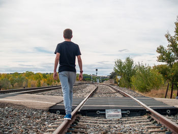 Rear view of man standing on railroad track against sky