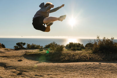 Full length of man jumping against sea on sunny day