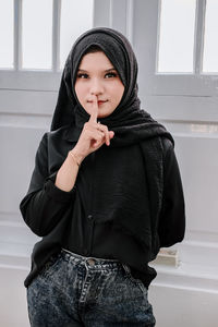 Portrait of young woman standing against wall