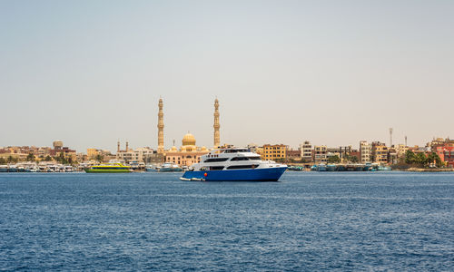 Sailboats in sea by buildings against clear sky