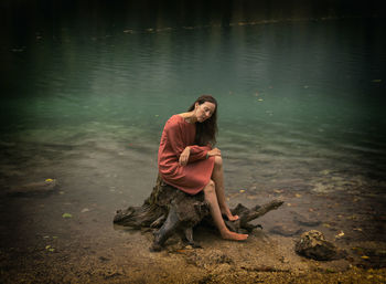 Woman in orange dress sitting on a log on the shore of a lake, italy iv
