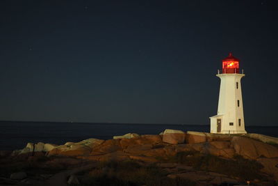 Lighthouse by sea against sky at night