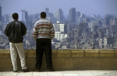 Rear view of men standing by railing against city buildings