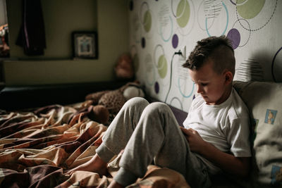 Rear view of boy sitting on bed at home