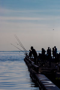 Silhouette people fishing in sea against sky during sunset