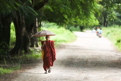 Monk walking with umbrella on road