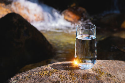 Drinking transparent water in a glass glass stands on a stone outdoors in a forest in nature, a