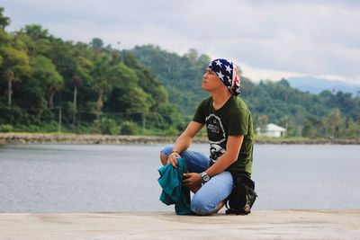 Man wearing bandana while kneeling on pier over lake