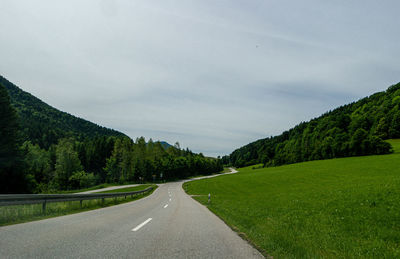 Empty road along trees and mountains against sky