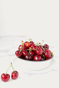 Fresh ripe red cherry with stalks in white ceramic pot placed on marble table against white wall