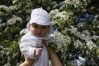 Cropped hands of parent holding son against flowering tree