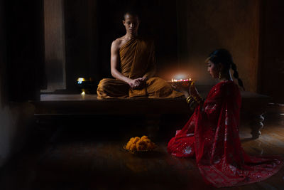 Side view of woman giving religious offering to monk in temple