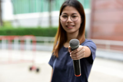 Portrait of female journalist with microphone standing against building
