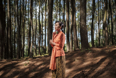 Woman standing by tree trunk in forest