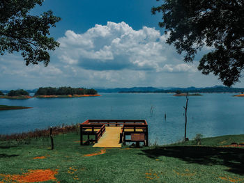 Empty bench by lake against sky