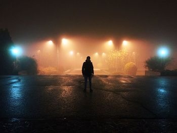 Man standing on street against illuminated street light at night