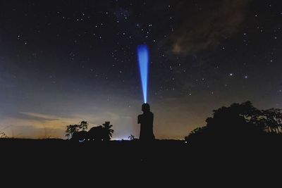 Silhouette man standing by tree against sky at night