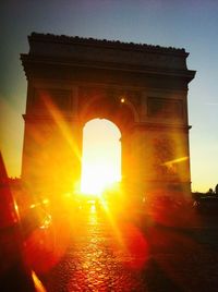 Sun shining through arch in city at sunset