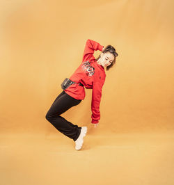 Full length portrait of woman standing against orange wall